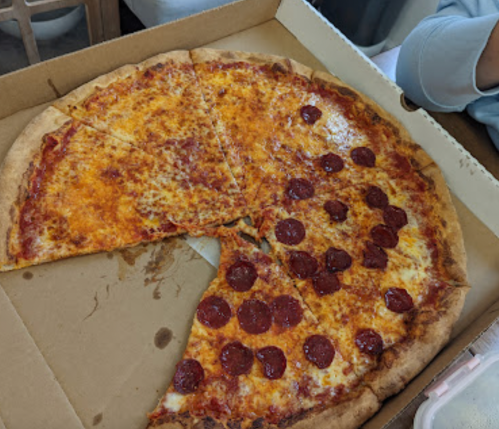 A pizza in a box with one slice missing, topped with cheese and pepperoni on one half.