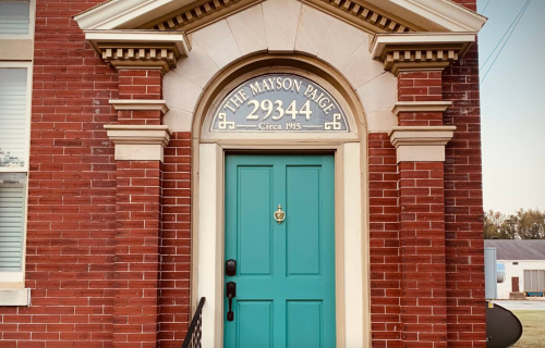 A teal door with a decorative arch, featuring the text "The Mayson Paige 29344 Circa 1915" above it, set in a brick wall.