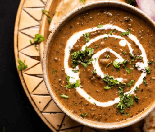 A bowl of lentil soup garnished with cream and fresh herbs, served on a decorative plate.