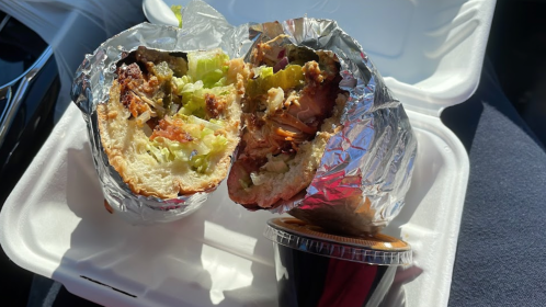 A partially eaten sandwich wrapped in foil, with lettuce and other fillings, next to a small container of sauce.