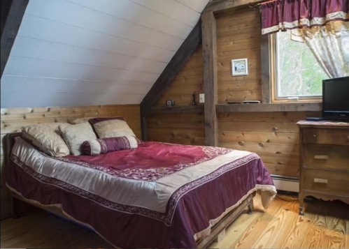 Cozy bedroom with a wooden interior, featuring a double bed, a dresser, and a window with curtains.