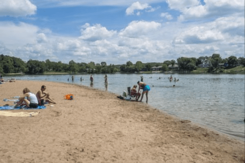 A sandy beach with people swimming and relaxing by the water under a partly cloudy sky.