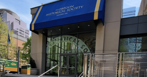 Entrance of the Oregon Historical Society, featuring a blue awning and steps leading up to the glass doors.