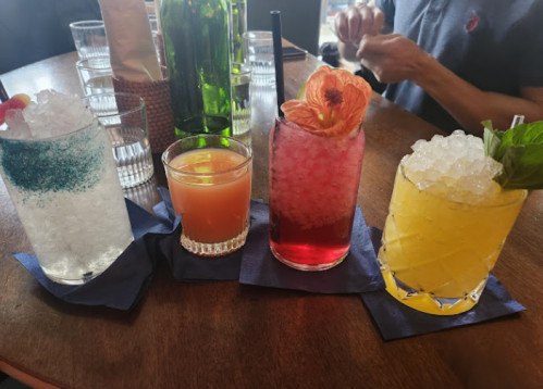Four colorful cocktails on a wooden table, each with unique garnishes and ice, served on blue napkins.