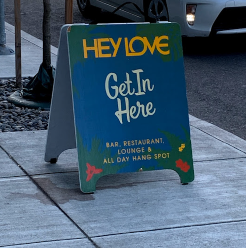 A colorful sign reads "Hey Love, Get In Here" promoting a bar, restaurant, and lounge.