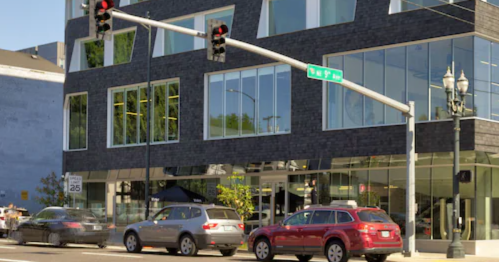 Modern black building with large windows, located at a street intersection on a clear day.