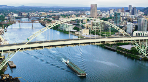 Aerial view of a city skyline with a bridge over a river, featuring boats and green spaces along the waterfront.