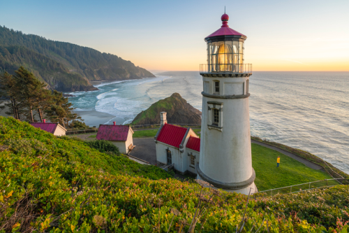 A scenic lighthouse on a cliff overlooking the ocean, surrounded by lush greenery and a sunset sky.
