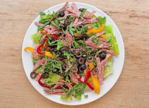 A colorful salad with lettuce, sliced salami, olives, and bell peppers on a white plate.
