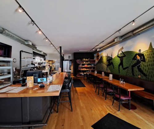 A cozy café interior with wooden floors, tables, and a counter displaying various baked goods and drinks.