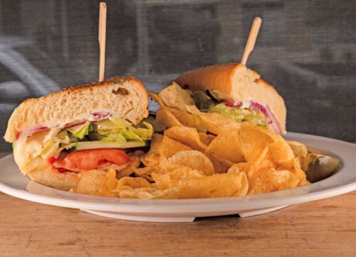 A plate with two sandwiches topped with lettuce and tomato, accompanied by a side of crispy potato chips.
