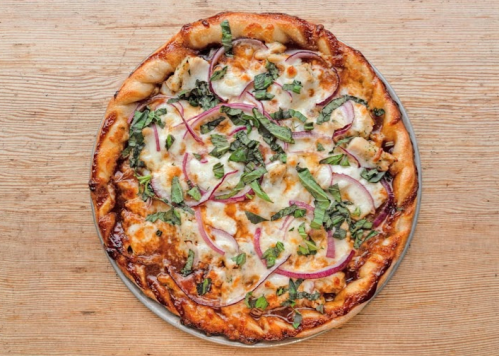 A freshly baked pizza topped with mozzarella, red onions, and fresh basil on a wooden surface.