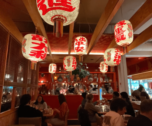 Cozy restaurant interior with red paper lanterns, wooden beams, and diners enjoying their meals.