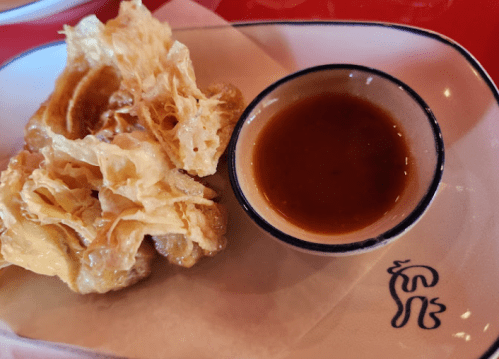 Crispy fried dish served with a small bowl of dipping sauce on a plate.