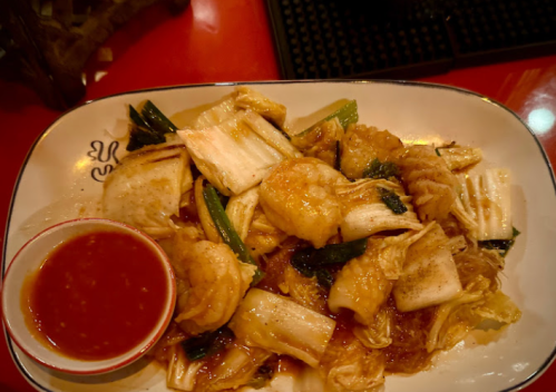 A plate of stir-fried vegetables and dumplings, served with a small bowl of dipping sauce.