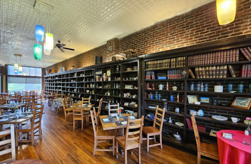 Cozy restaurant interior with wooden tables, shelves filled with vintage items, and colorful pendant lights.