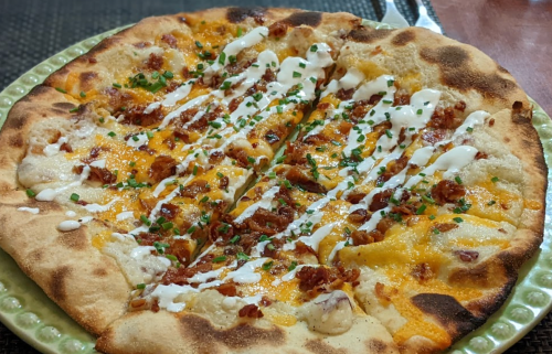 A freshly baked pizza topped with cheese, bacon, and drizzled with white sauce, garnished with green onions.