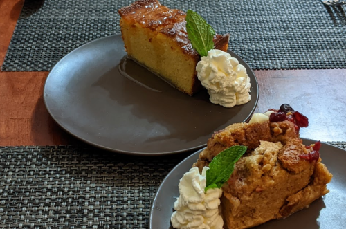 Two dessert plates: one with a slice of cake and the other with a bread pudding, both topped with whipped cream and mint.