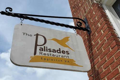 Sign for The Palisades Restaurant in Eggleston, VA, featuring a hummingbird design and a brick wall background.