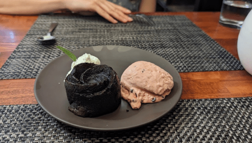 A plate with three scoops of ice cream: black, pink with chocolate chips, and green, on a textured table setting.