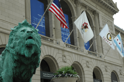 A green lion statue in front of a building with flags and banners, including the American flag and city flags.