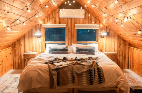 Cozy attic bedroom with a large bed, wooden walls, and string lights creating a warm ambiance.