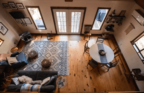 A cozy living space with a large rug, a round dining table, and wooden chairs, featuring natural light from double doors.