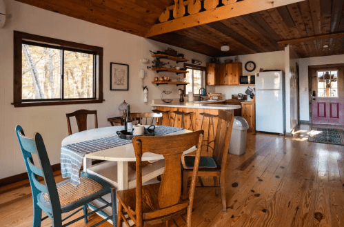 Cozy kitchen and dining area with wooden accents, a round table, and a mix of chairs, bathed in natural light.