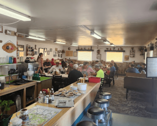 A cozy diner filled with patrons enjoying meals, featuring a rustic decor and a counter with stools.