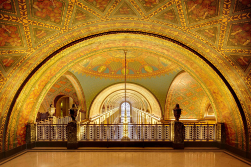 Ornate archway with colorful floral patterns and intricate designs, leading to a grand staircase and illuminated windows.
