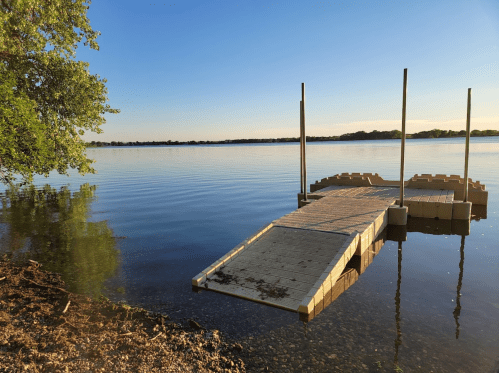A serene lake view with a wooden dock extending into calm waters under a clear blue sky.