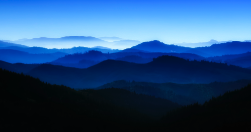 A serene landscape of layered blue mountains under a gradient sky, creating a tranquil and atmospheric scene.