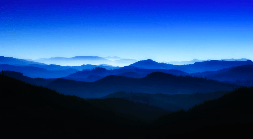 A serene landscape of layered blue mountains under a gradient sky, creating a tranquil and atmospheric scene.