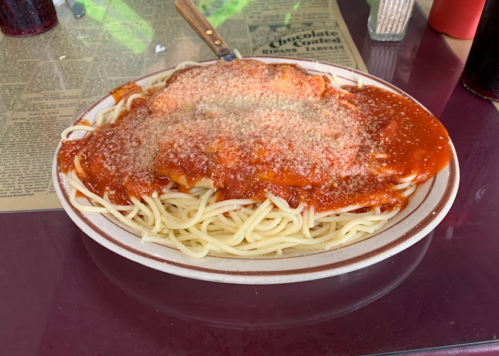 A plate of spaghetti topped with marinara sauce and grated cheese, served on a table with a menu in the background.