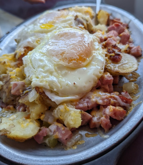 A sizzling plate of hash browns topped with ham and two sunny-side-up eggs.