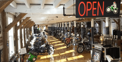 A spacious motorcycle museum with various bikes on display and an "OPEN" sign illuminated.
