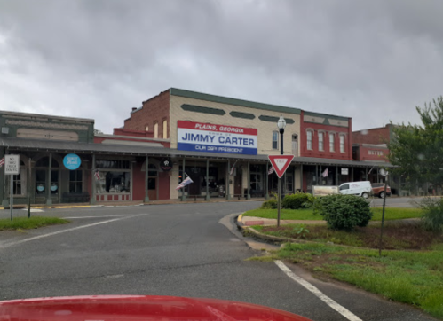 A small town street in Plains, Georgia, featuring a building with a sign for "Jimmy Carter" and cloudy skies.