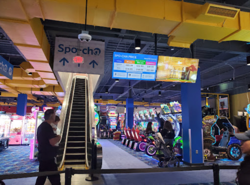 Interior of an arcade with an escalator, colorful game machines, and a digital price display.