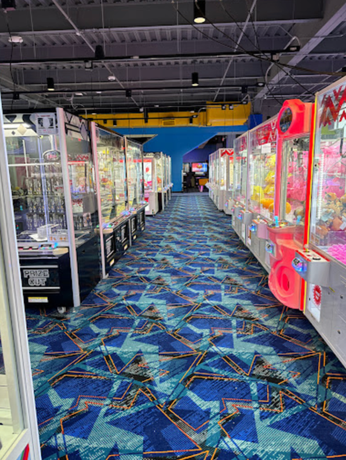 A colorful arcade with rows of claw machines and a vibrant patterned carpet.