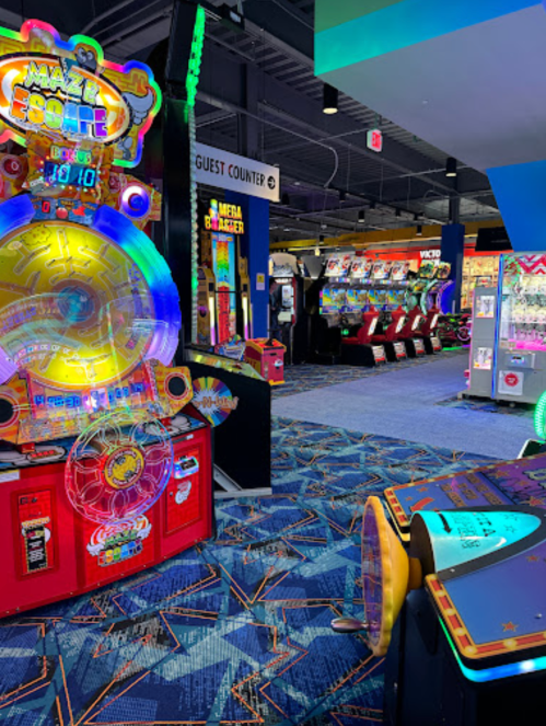 Brightly lit arcade with colorful games, including a large ticket redemption machine and various other gaming stations.