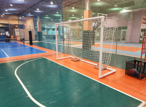 Indoor sports facility featuring a soccer goal, basketball hoop, and multi-colored court surfaces.