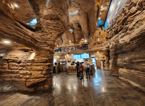 Interior of a cave-like space with rock formations, a reception area, and visitors exploring the unique environment.