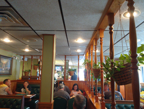 Interior of a cozy restaurant with wooden accents, hanging plants, and patrons dining at tables.