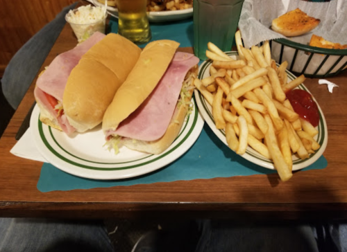 A plate with two ham sandwiches and a side of French fries with ketchup on a wooden table.