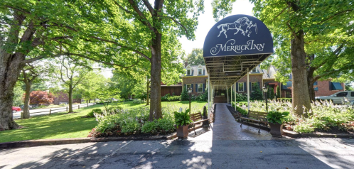 A charming inn entrance surrounded by lush greenery and trees, featuring a covered walkway and well-maintained landscaping.