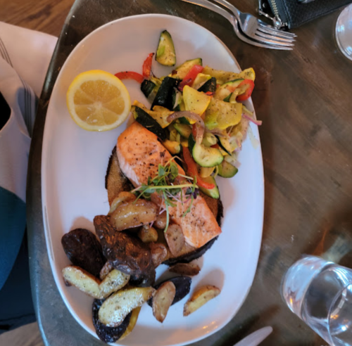 A plate featuring grilled salmon, roasted potatoes, and sautéed vegetables, garnished with a lemon slice.
