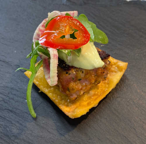 A gourmet appetizer featuring a crispy base topped with seasoned meat, fresh greens, and sliced peppers.
