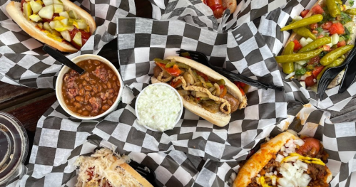 A variety of hot dogs with toppings, sides of baked beans and coleslaw, all served in checkered paper.