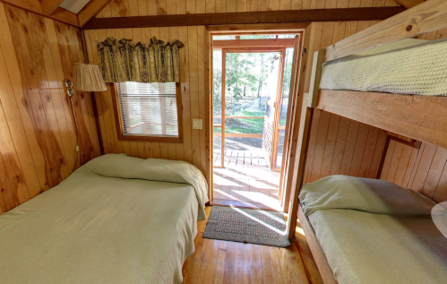 Cozy wooden cabin interior with a double bed, bunk beds, and a door leading to an outdoor deck.