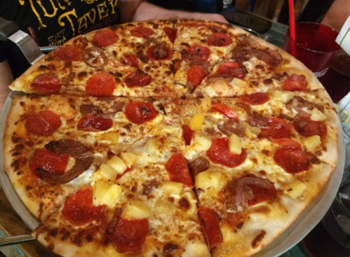 A large pizza topped with pepperoni, pineapple, and sausage, served on a metal tray.